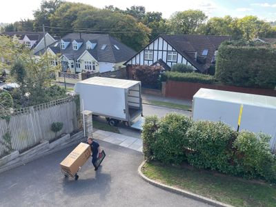 A man moving a large box on a trolley near parked trucks in a residential area.