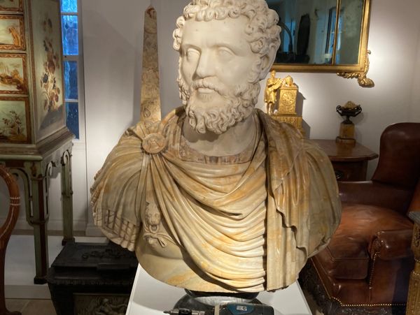 Marble bust of a bearded man with draped clothing in a decorated room.