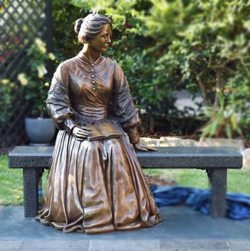 Bronze statue of a Victorian woman sitting on a bench with a book.