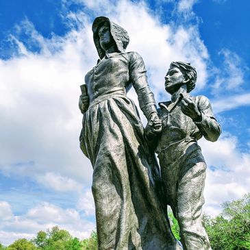 Statue of a woman and child holding hands against a blue sky.