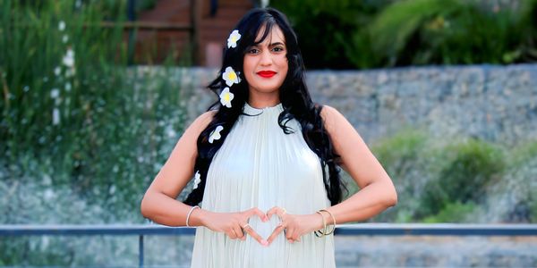 Woman in white dress making a heart shape with her hands outdoors.