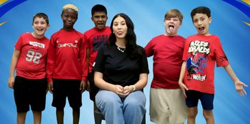 A woman sits with five excited boys against a blue backdrop.