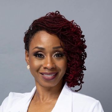 Confident woman with styled red dreadlocks and white blazer smiles warmly.