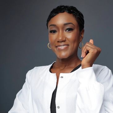 Confident woman in white jacket smiling against gray background.