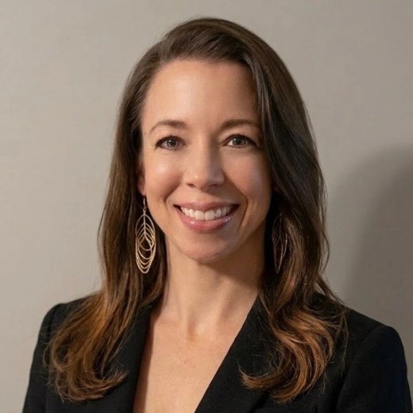 Professional woman with long brown hair smiling, wearing a black blazer and statement earrings.