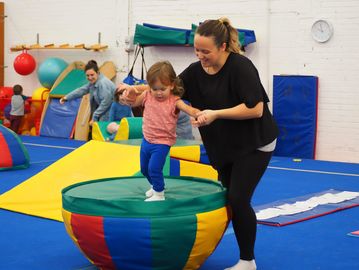 Child balancing on a colorful padded object with adult assistance.