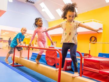 Children balancing on a gym beam indoors.