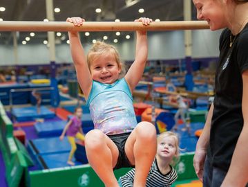 Child happily hanging from a bar in a gym.