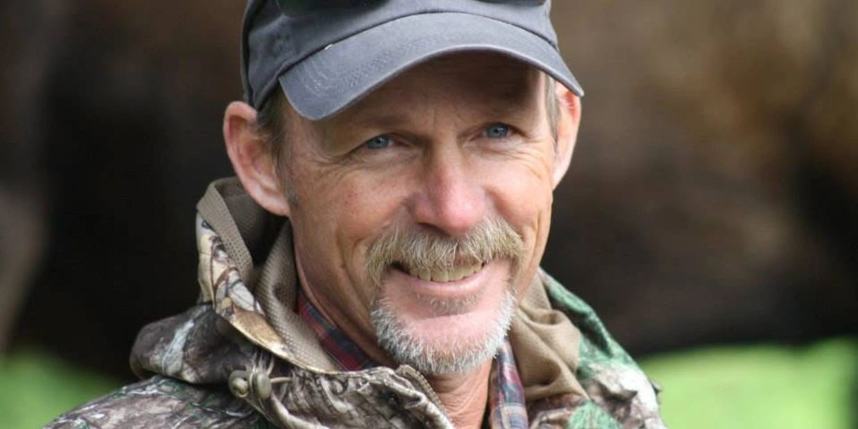 Smiling man in camouflage jacket and cap.