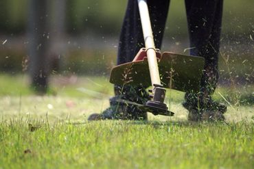 Person using a string trimmer to cut grass outdoors.