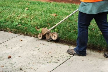 Person using a lawn edger to trim grass along a sidewalk.