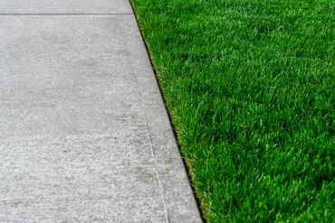 A clean concrete sidewalk next to a lush green lawn.