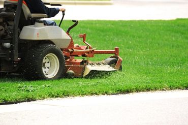 A person mowing a green lawn with a riding mower.