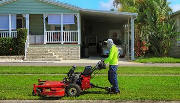 Person mowing a lawn in bright clothing in front of a house.