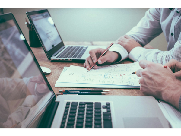 Two people collaborating with laptops and notes on a wooden table.