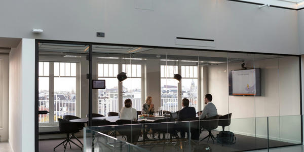 Four people having a meeting in a glass-walled conference room with city views.