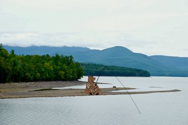 A bear fishing by a lake with mountains in the background.