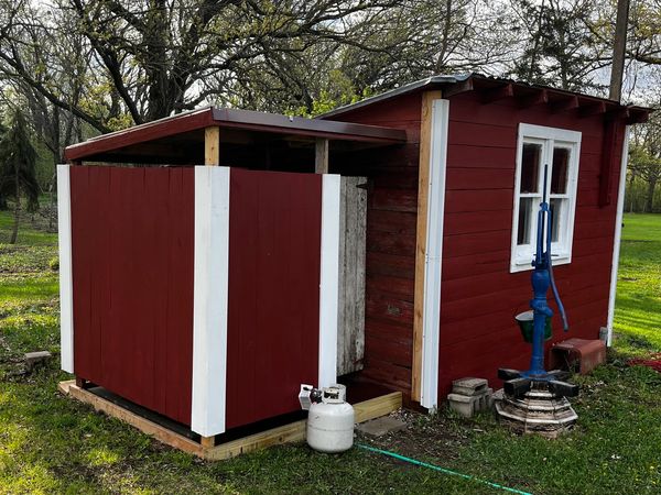 Small red wooden shed with a propane tank and outdoor water pump.