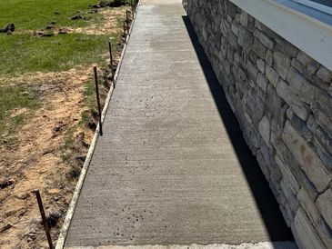 Newly poured concrete walkway along a house with stone siding.