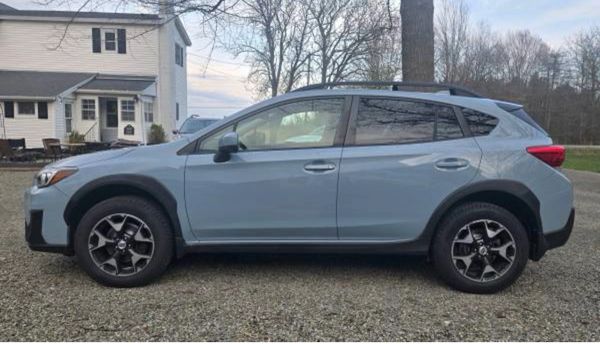 Side view of a blue crossover SUV parked on gravel in front of a house.