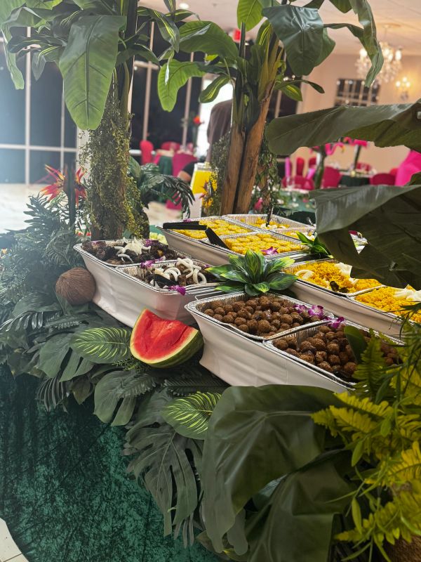 Buffet table with tropical-themed food presentation and foliage.