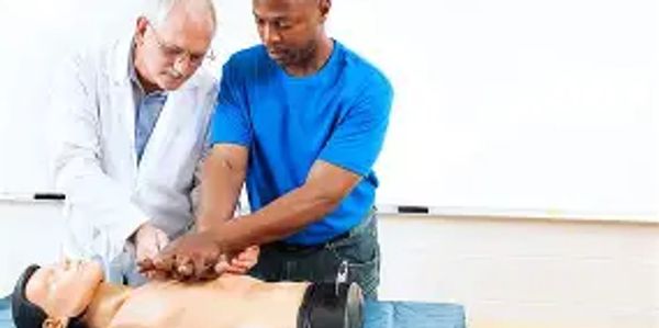 A man learns CPR chest compressions on a training mannequin with instructor guidance.