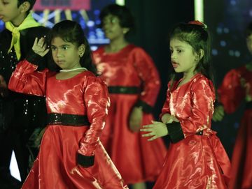 Children performing a dance in vibrant red costumes on stage.