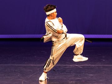 Young dancer in silver outfit striking a dynamic pose on stage.