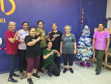 A group of women posing happily in a dance studio with a decorated white Christmas tree.
