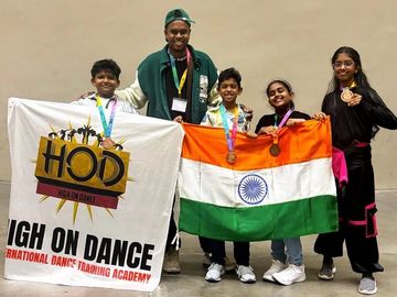 Group of young dancers proudly holding medals, Indian flag, and a dance academy banner.