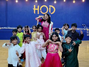 A group of children and a woman posing happily in colorful traditional attire in a dance studio.