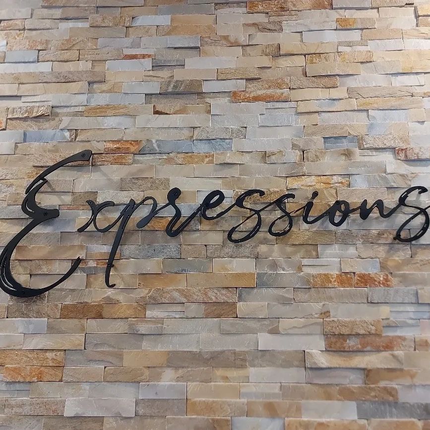 Black cursive 'Expressions' sign on a textured stone wall.