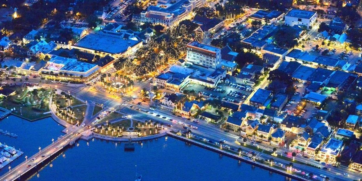 Aerial night view of a vibrant waterfront town with illuminated streets and buildings.