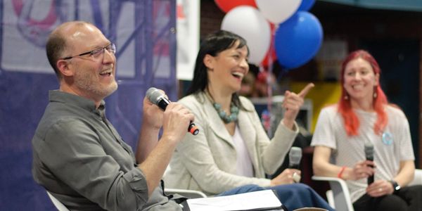 Andy Hoover, Elizabeth Randol, and Molly Tack-Hooper sit on a stage, holding microphones.