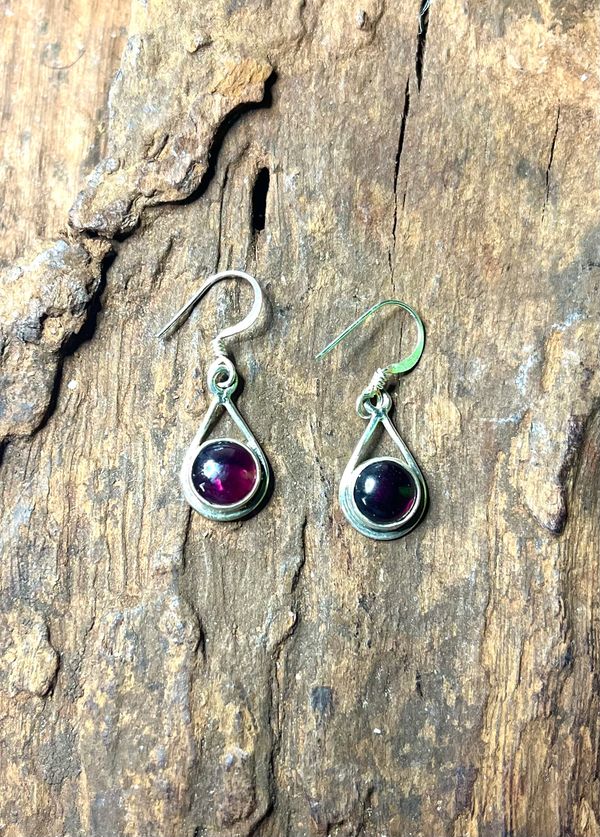 Pair of silver earrings with dark purple stones on wood.