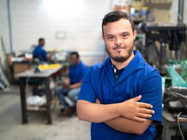 Man in a blue shirt smiling with crossed arms in a workshop.