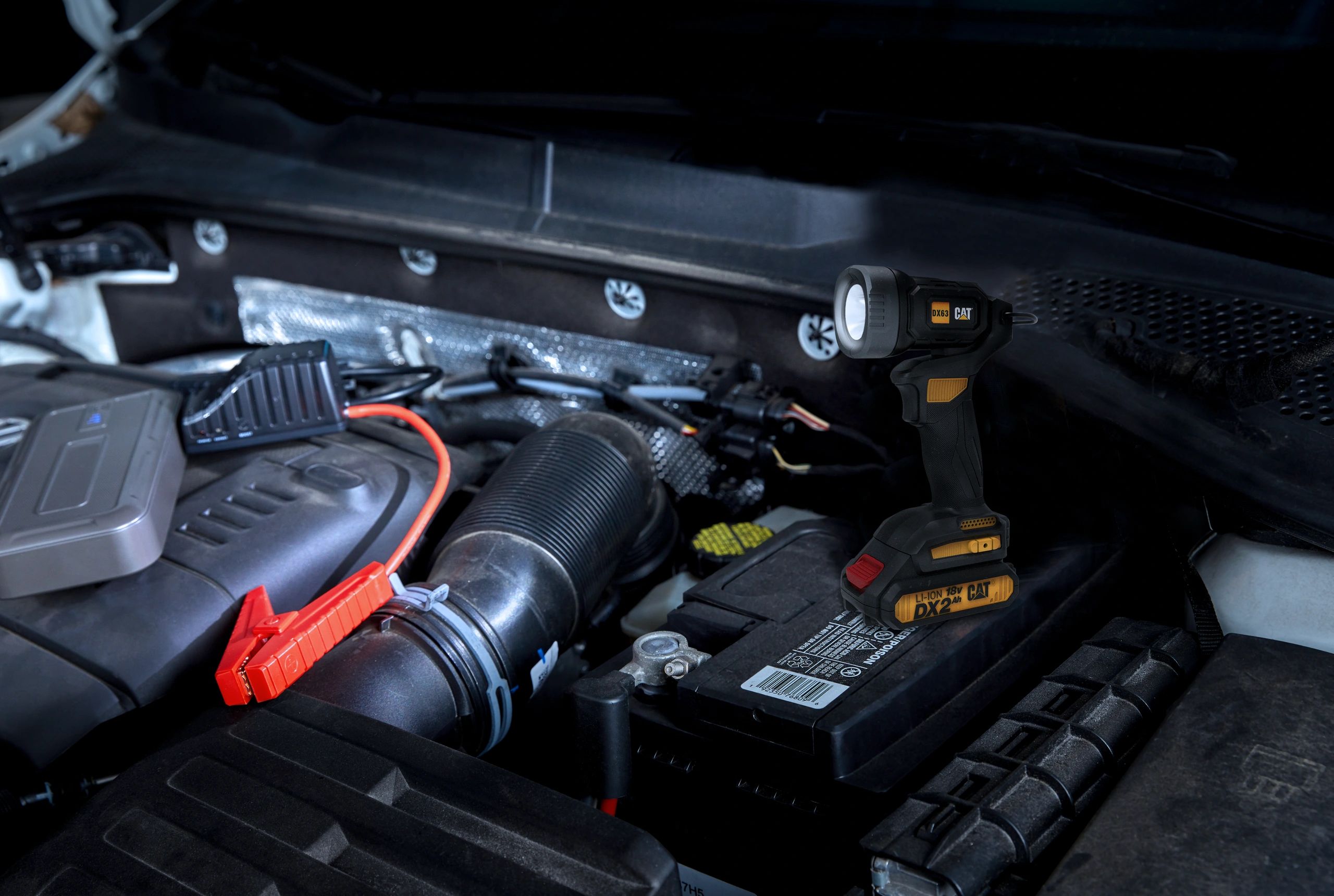 Portable CAT DX63 work light illuminating a car engine bay during maintenance.