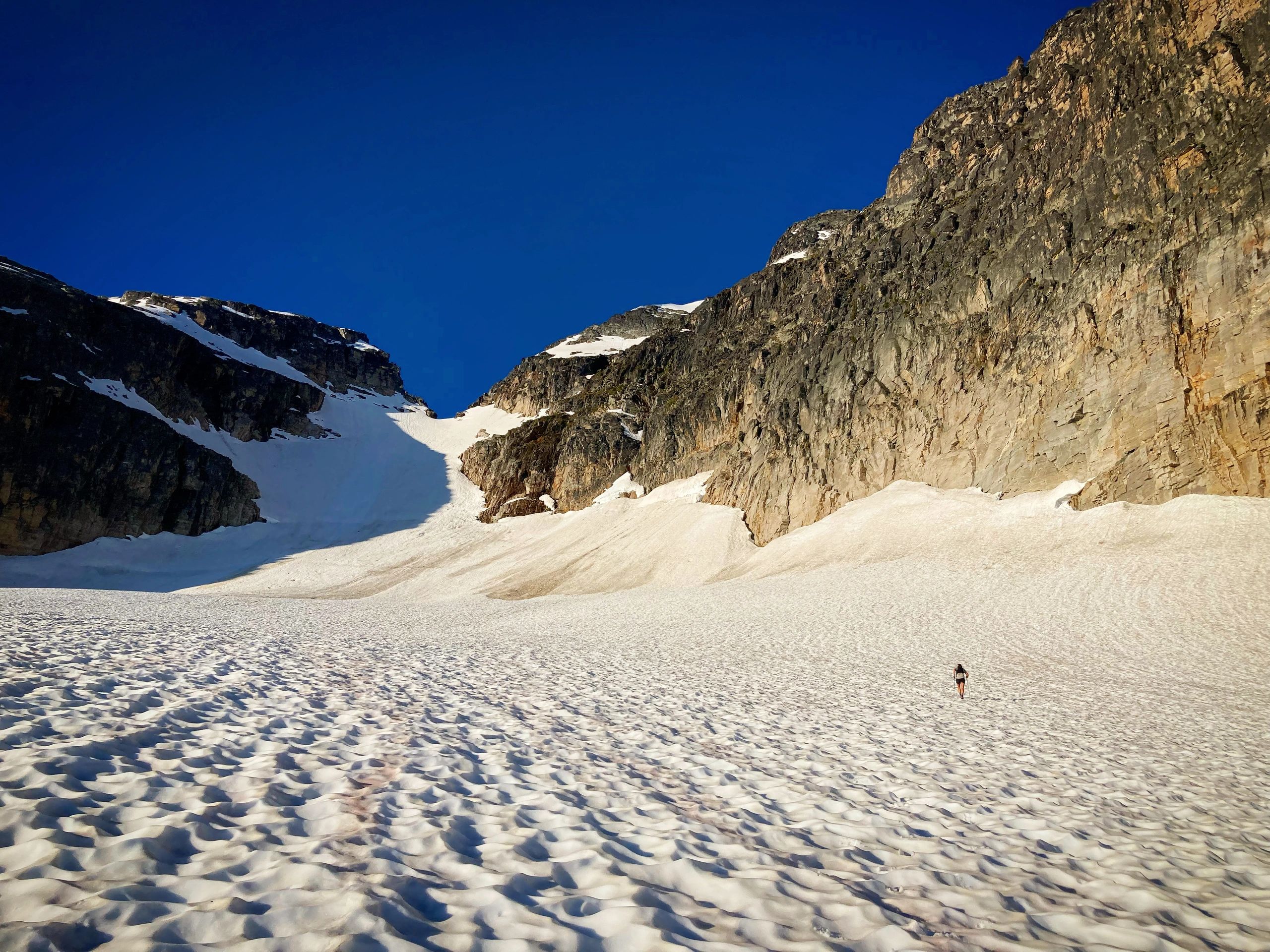 A lone person hiking on a snowy mountain under a clear blue sky.