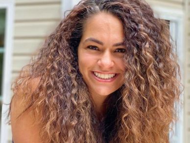 Smiling woman with voluminous curly hair outdoors.