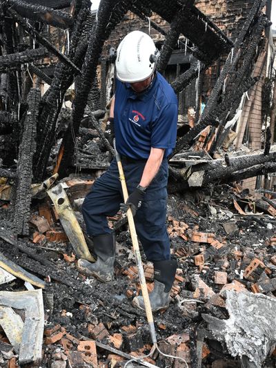Worker in protective gear inspecting charred remains after a fire.