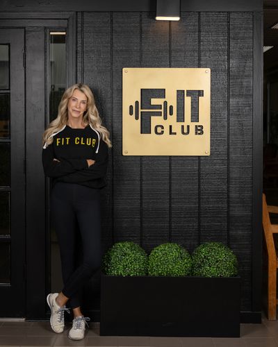 Woman standing confidently by a Fit Club sign on a black wall.