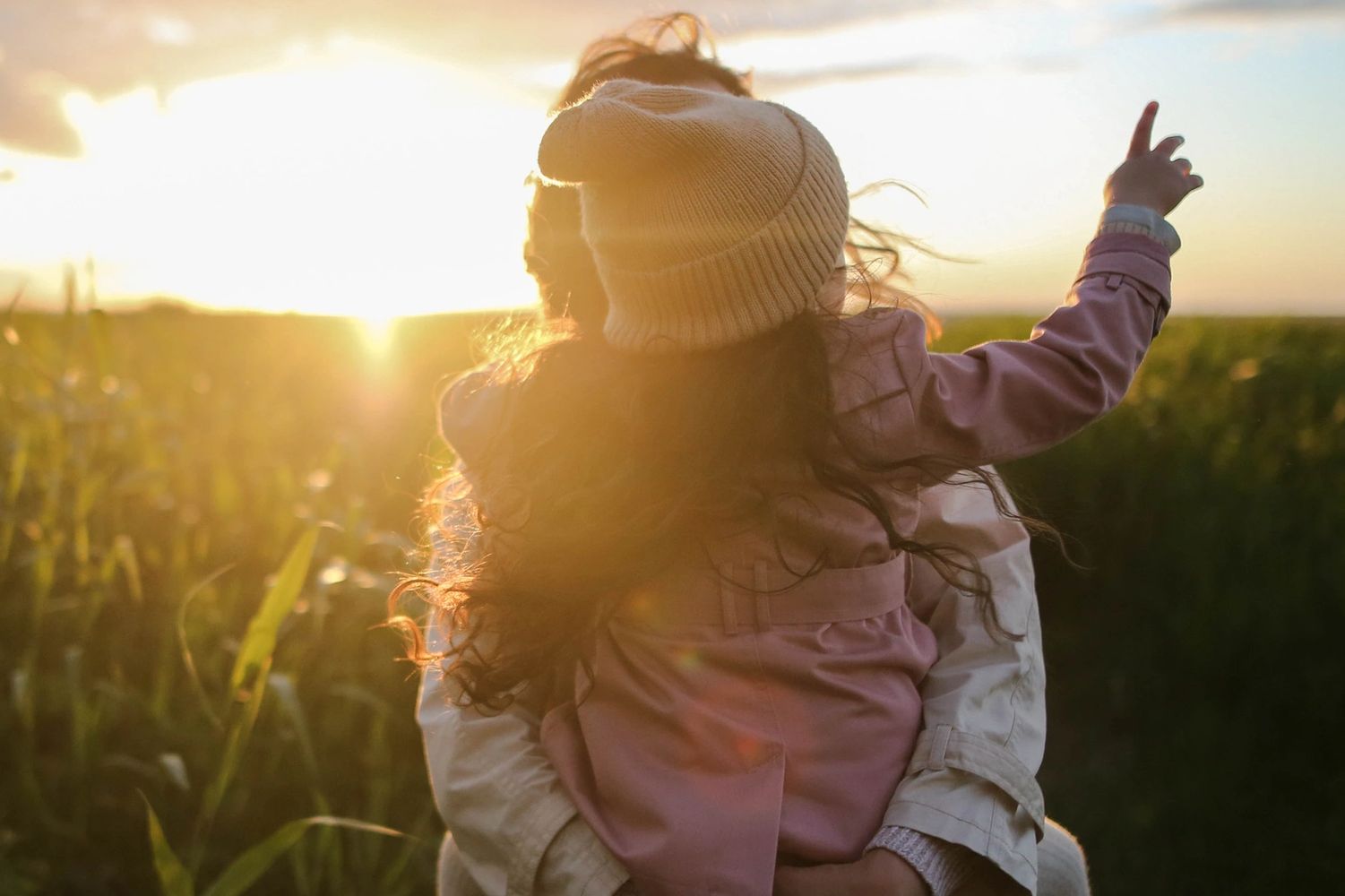 Parent holding girl on her back while walking outside in the sunshine