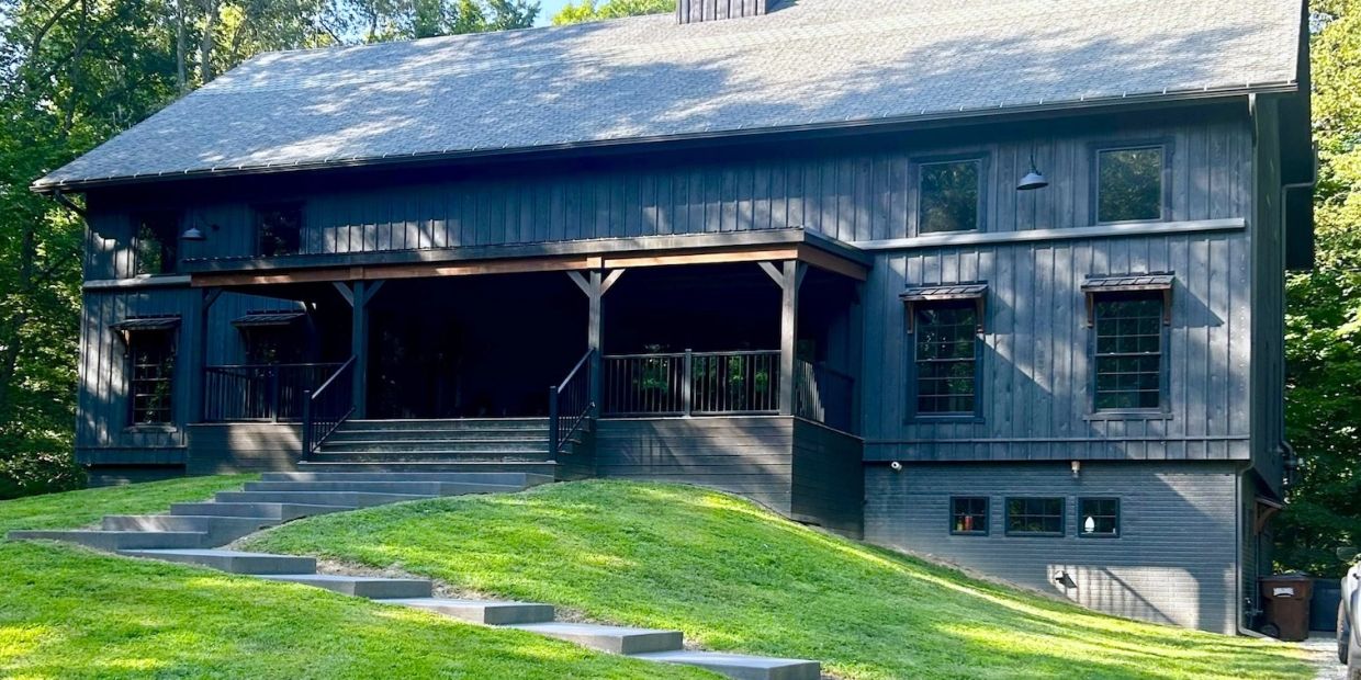Modern dark wooden house with stairs and green lawn.