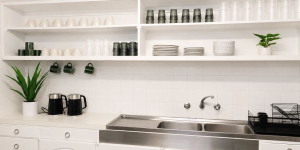 Organized kitchen shelves with cups, plates, kettles, plants, and a sink.
