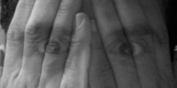 Eyes visible through fingers covering the face.