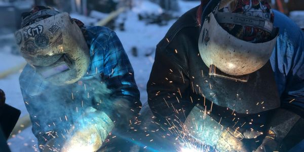 Two welders working outdoors, sparks flying from their welding torches.