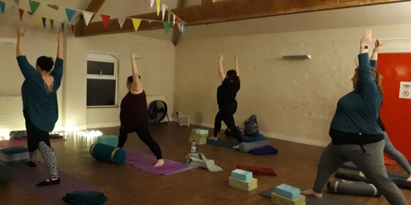 Group practicing yoga in a studio with raised arms.