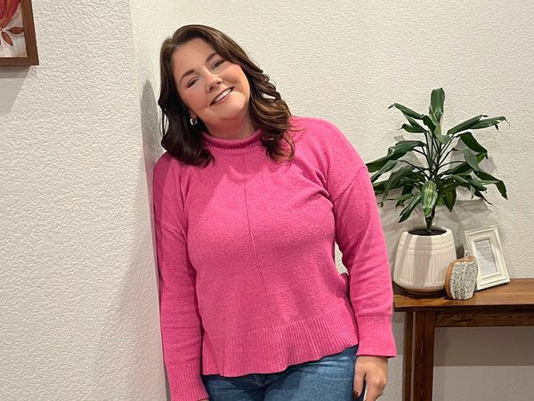 Smiling woman in pink sweater leaning against wall.