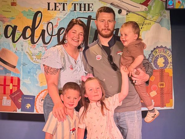 Smiling family of five posing in front of travel-themed backdrop.