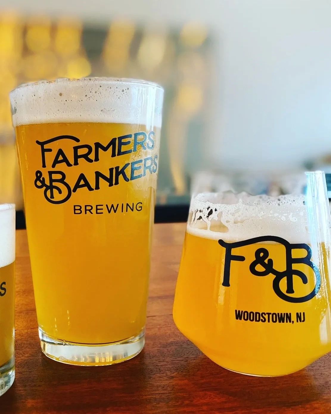 Two glasses of beer from Farmers &amp; Bankers Brewing on a wooden table.